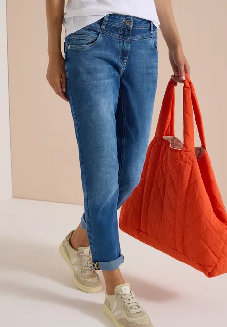 Person trägt hochgekrempelte Jeans, goldene Sneaker und hält eine orange Stepp-Tasche.