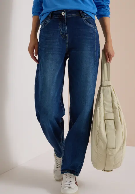 Eine Person trägt blaue Jeans, weiße Sneaker und hält eine helle, gesteppte Tragetasche.