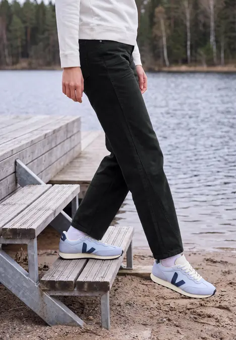 Person trägt schwarze Hose und weiße Sneaker auf hölzerner Treppe am Ufer eines Sees.