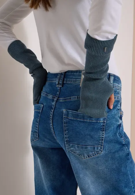 Person trägt lange, grüne, fingerlose Handschuhe und blaue Jeans, Rückansicht.