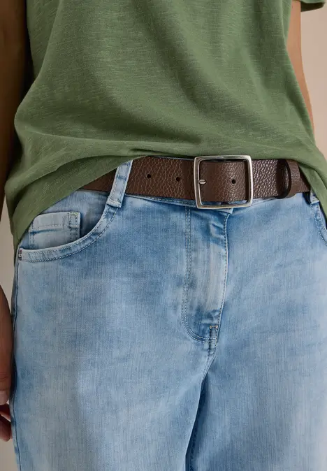 Person trägt grünes T-Shirt, helle Jeans und braunen Gürtel mit eckiger Metallschnalle.