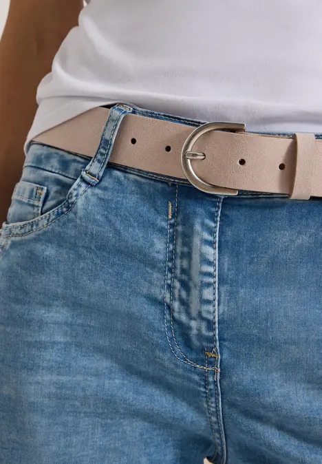 Taillenansicht: hellbeiger Gürtel mit silberner Schnalle über blauen Jeans und weißem Oberteil.