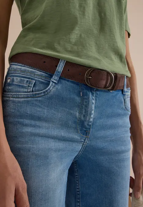 Nahaufnahme einer Person mit grünem Oberteil, blauen Jeans und braunem Gürtel.