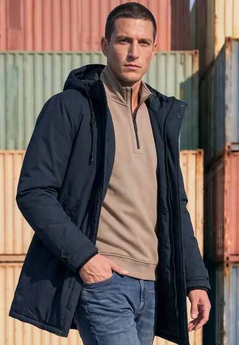 Ein Mann in dunkler Jacke und Jeans steht vor gestapelten bunten Container-Boxen.