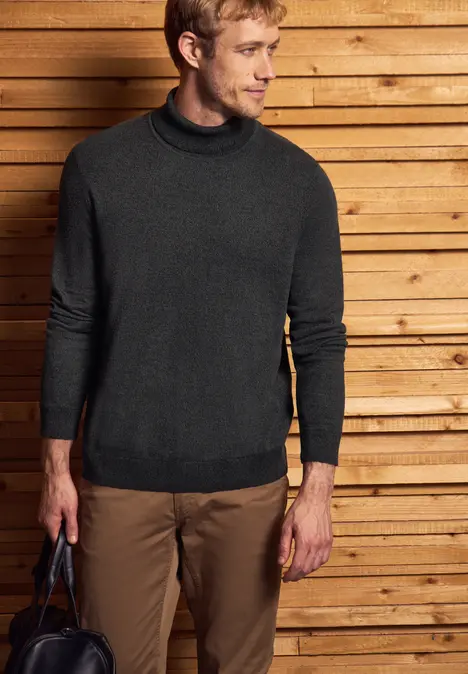 Mann im dunklen Rollkragenpullover vor Holzwand.