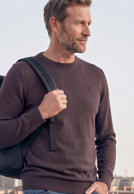 Un homme porte un sac à dos et un pull devant un paysage urbain.
