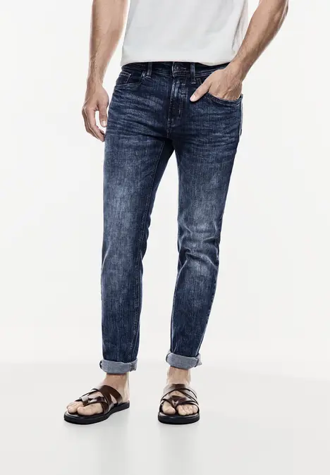 Mann trägt Jeans, weißes Shirt und Sandalen.