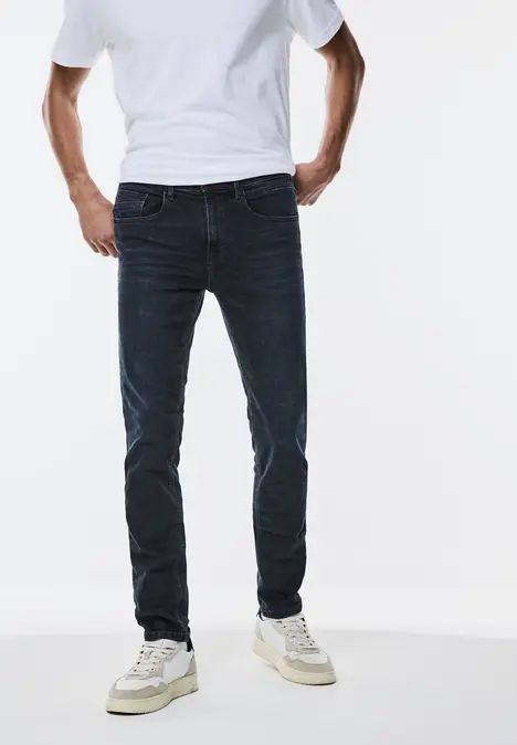 Mann trägt weißes T-Shirt, dunkle Jeans und weiße Sneaker.