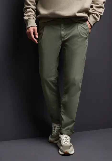 Mann trägt grüne Hose, beigen Pullover und Turnschuhe.