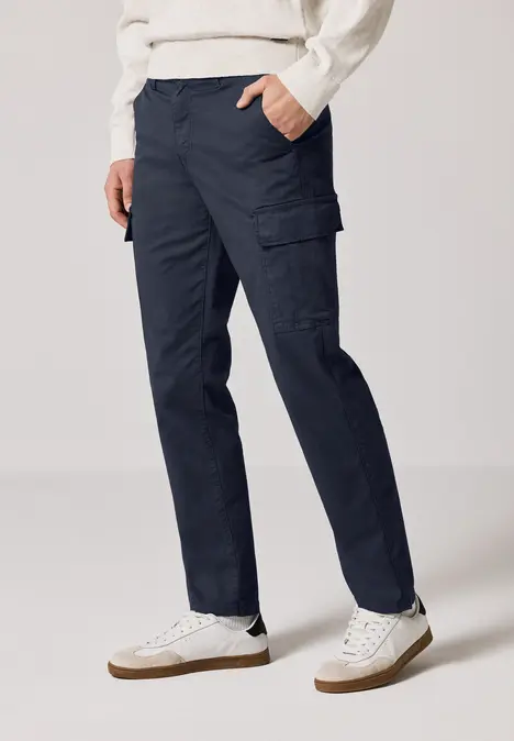 Person trägt dunkelblaue Cargohose und weiße Turnschuhe.