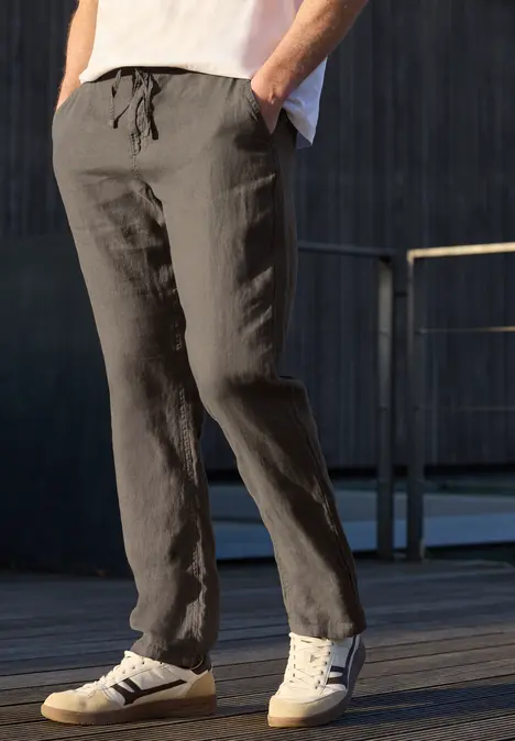 Mann trägt lässige graue Leinenhose und weiße Sneaker, steht draußen auf Holzboden.