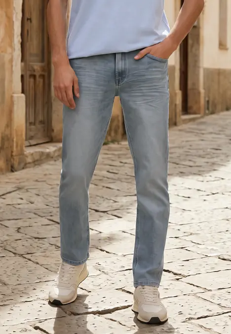Person trägt hellblaue Jeans und weiße Sneaker, steht mit Hand in Tasche auf Kopfsteinpflaster.