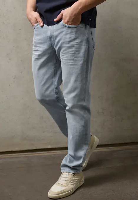 Eine Person trägt hellblaue Jeans und weiße Sneakers vor grauer Betonwand.