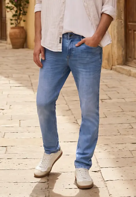 Ein Mann trägt hellblaue Jeans und weiße Sneaker auf gepflastertem Weg.